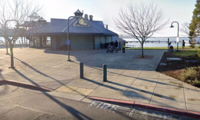 Waterfront park with a blue-roofed pavilion, leafless trees, and people strolling near the pier.