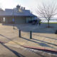Waterfront park with a blue-roofed pavilion, leafless trees, and people strolling near the pier.