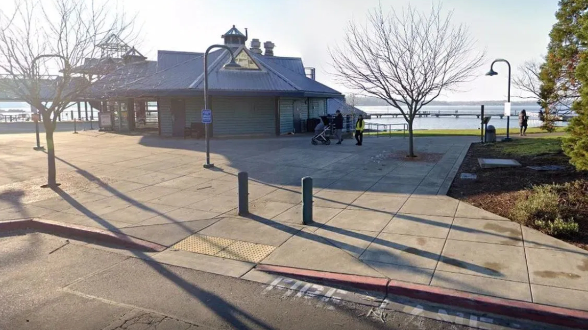 Waterfront park with a blue-roofed pavilion, leafless trees, and people strolling near the pier.