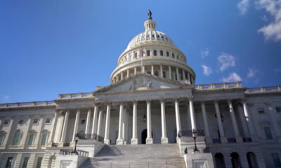 Front view of the U.S. Capitol with its dome, steps, and tall white columns against a blue sky.