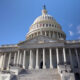Front view of the U.S. Capitol with its dome, steps, and tall white columns against a blue sky.