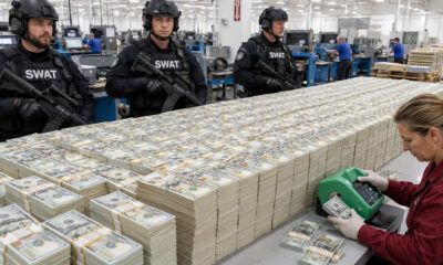 SWAT officers in tactical gear guard a currency processing area with huge stacks of bundled $100 bills and workers in the background.