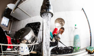 Water runs from a kitchen faucet into a sink full of dishes in a dish rack on the counter.