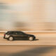 Dark station wagon speeding along a sunlit highway with motion blur.