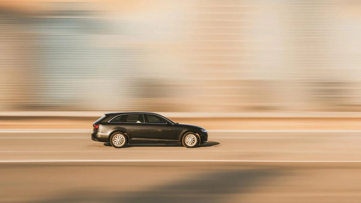Dark station wagon speeding along a sunlit highway with motion blur.