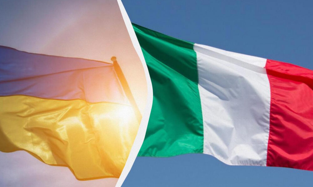 Two flags fluttering in the wind: a yellow flag with hints of red on the left and a green, white, and red flag on the right.