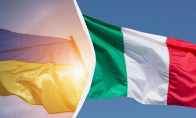 Two flags fluttering in the wind: a yellow flag with hints of red on the left and a green, white, and red flag on the right.