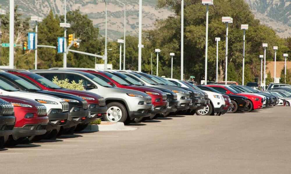 Row of cars parked in a dealership lot with mountains in the background.