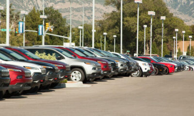 Row of cars parked in a dealership lot with mountains in the background.