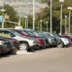 Row of cars parked in a dealership lot with mountains in the background.