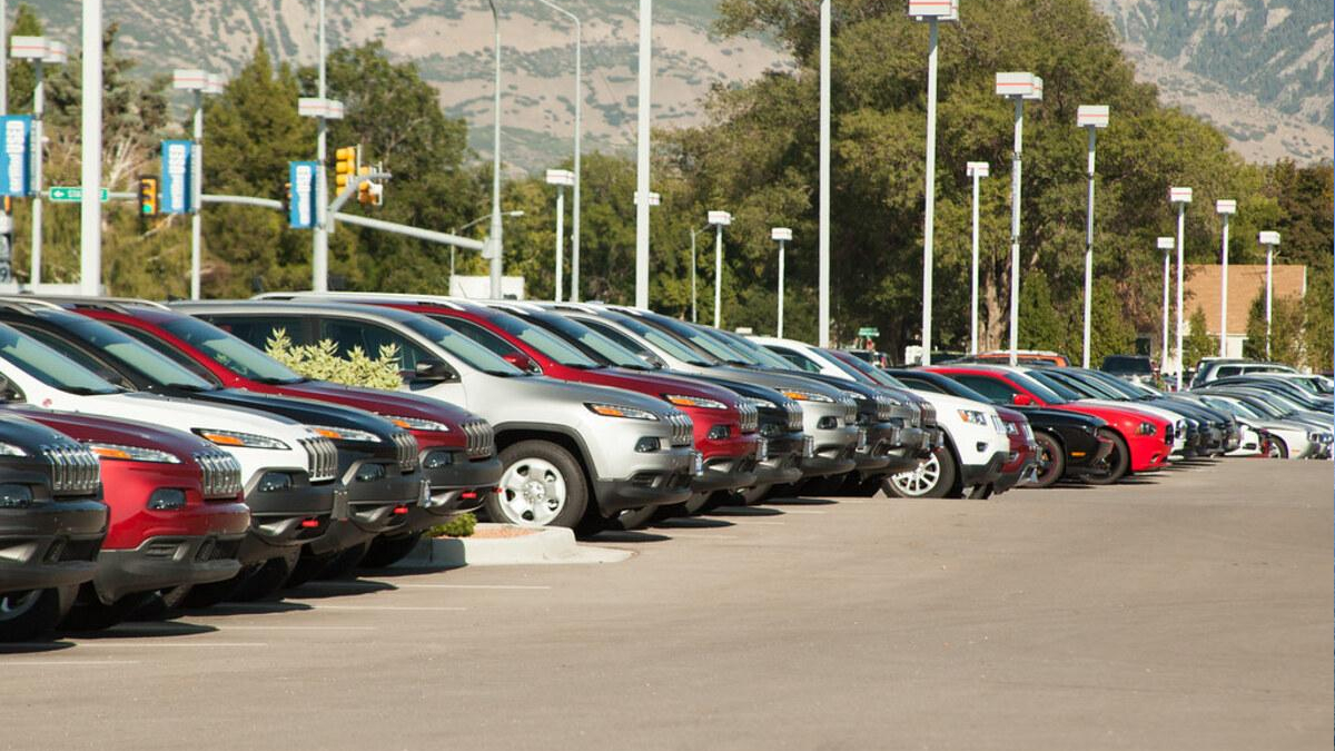 Row of cars parked in a dealership lot with mountains in the background.