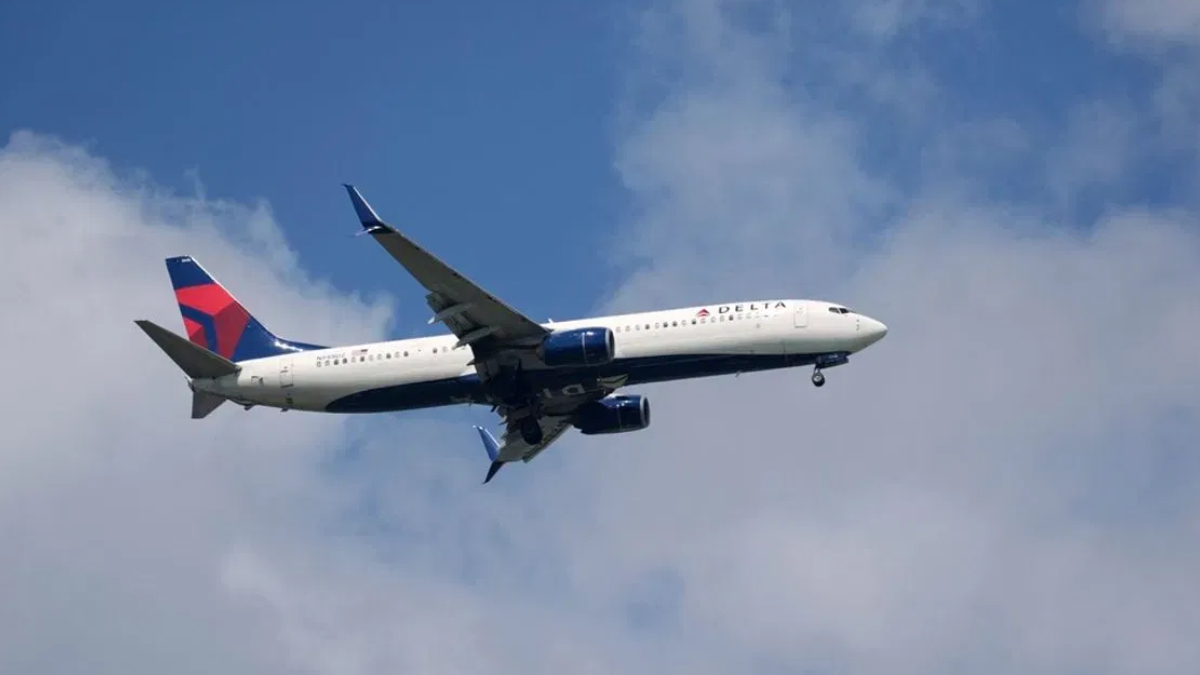 Delta Air Lines commercial jet in flight with landing gear down against blue sky and clouds