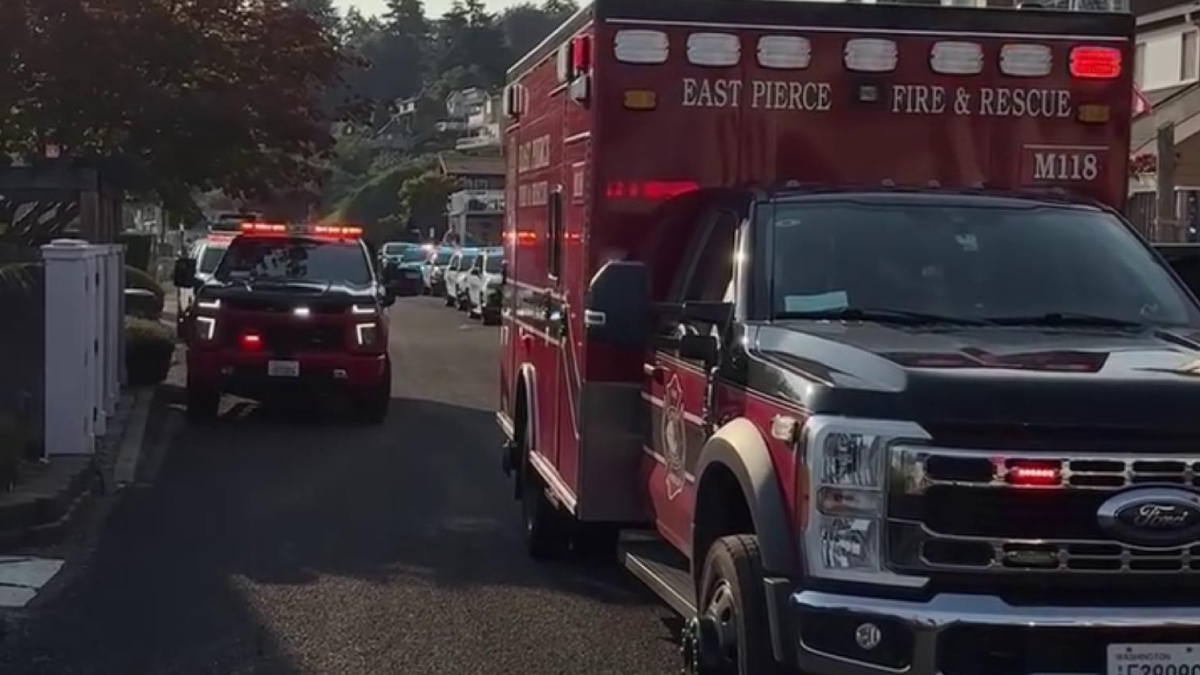 Front-right view of a red East Pierce Fire & Rescue ambulance with flashing lights, parked on a suburban street with other emergency vehicles in the background.