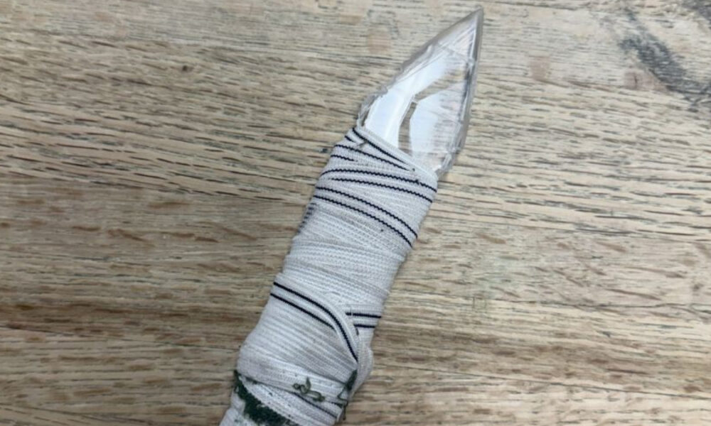 Knife with a striped cloth wrapped around the handle area, resting on a wooden surface.