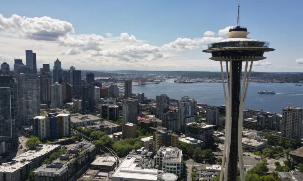 Seattle skyline with the Space Needle overlooking Puget Sound on a sunny day, city to the left and water to the right.