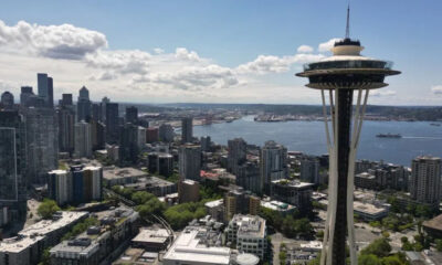 Seattle skyline with the Space Needle overlooking Puget Sound on a sunny day, city to the left and water to the right.