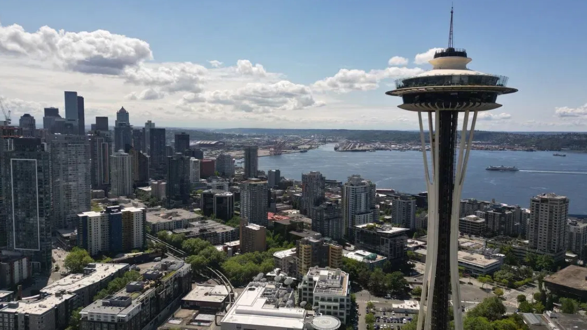 Seattle skyline with the Space Needle overlooking Puget Sound on a sunny day, city to the left and water to the right.