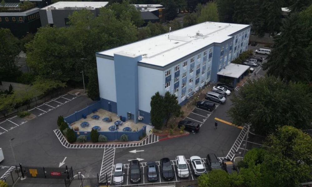 Aerial view of a light blue, three-story building with a gated parking lot and an outdoor seating area with blue tables and chairs.