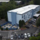 Aerial view of a light blue, three-story building with a gated parking lot and an outdoor seating area with blue tables and chairs.