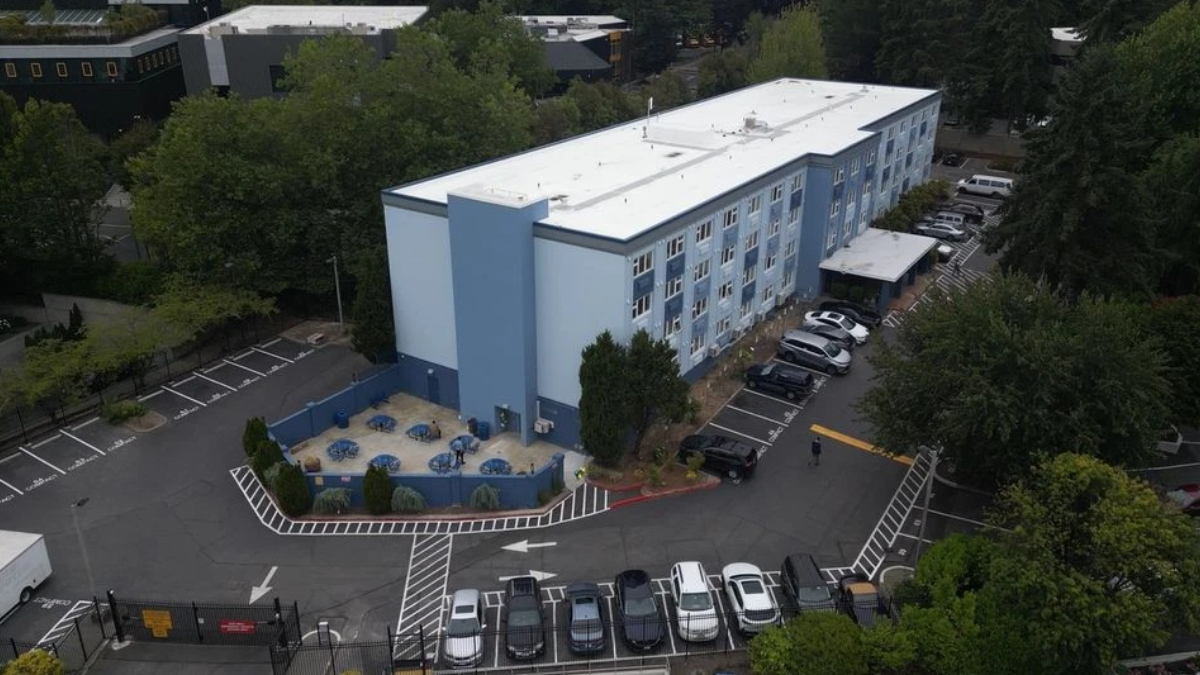 Aerial view of a light blue, three-story building with a gated parking lot and an outdoor seating area with blue tables and chairs.