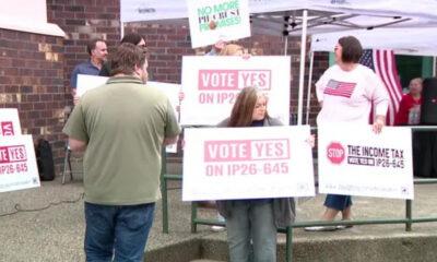 Group of people at an outdoor political rally holding signs reading 'Vote Yes on IP26-645'.