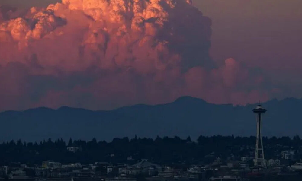 Seattle skyline at dusk with Space Needle against pink-orange clouds and distant hills, city lights below.