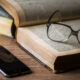 Glasses rest on an open book, with a smartphone on a wooden table nearby.