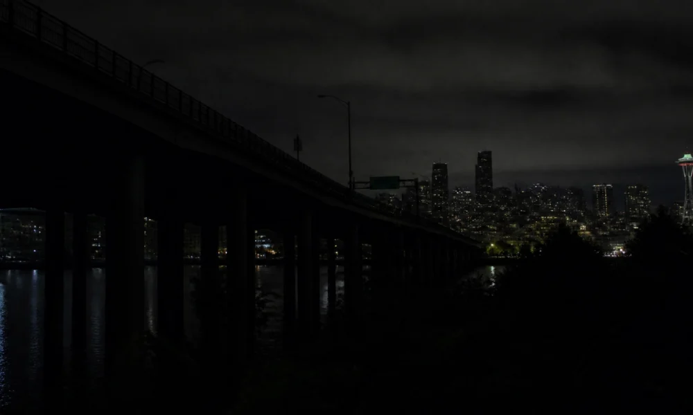 Nighttime city skyline with a bridge in the foreground and the illuminated Space Needle in Seattle.