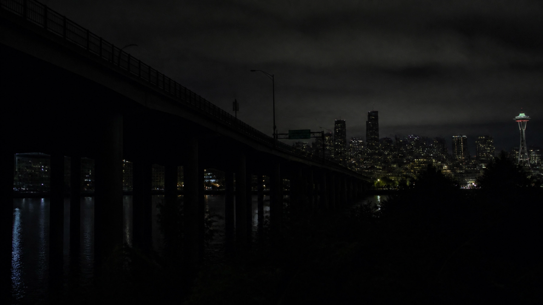 Nighttime city skyline with a bridge in the foreground and the illuminated Space Needle in Seattle.