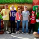 Two life-sized Mario & Luigi mascots flank a group of four visitors posing outdoors in a theme-park-like area.