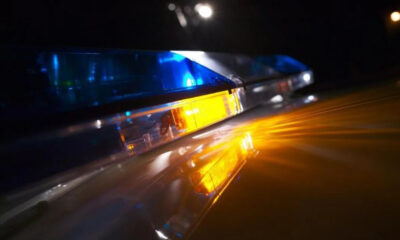 Nighttime police car with blue and amber emergency lights reflecting off a wet surface, creating dramatic glow and motion blur.