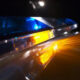 Nighttime police car with blue and amber emergency lights reflecting off a wet surface, creating dramatic glow and motion blur.