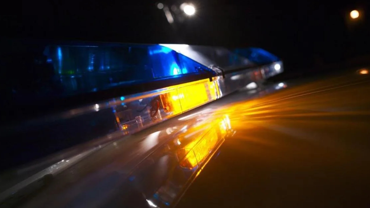 Nighttime police car with blue and amber emergency lights reflecting off a wet surface, creating dramatic glow and motion blur.