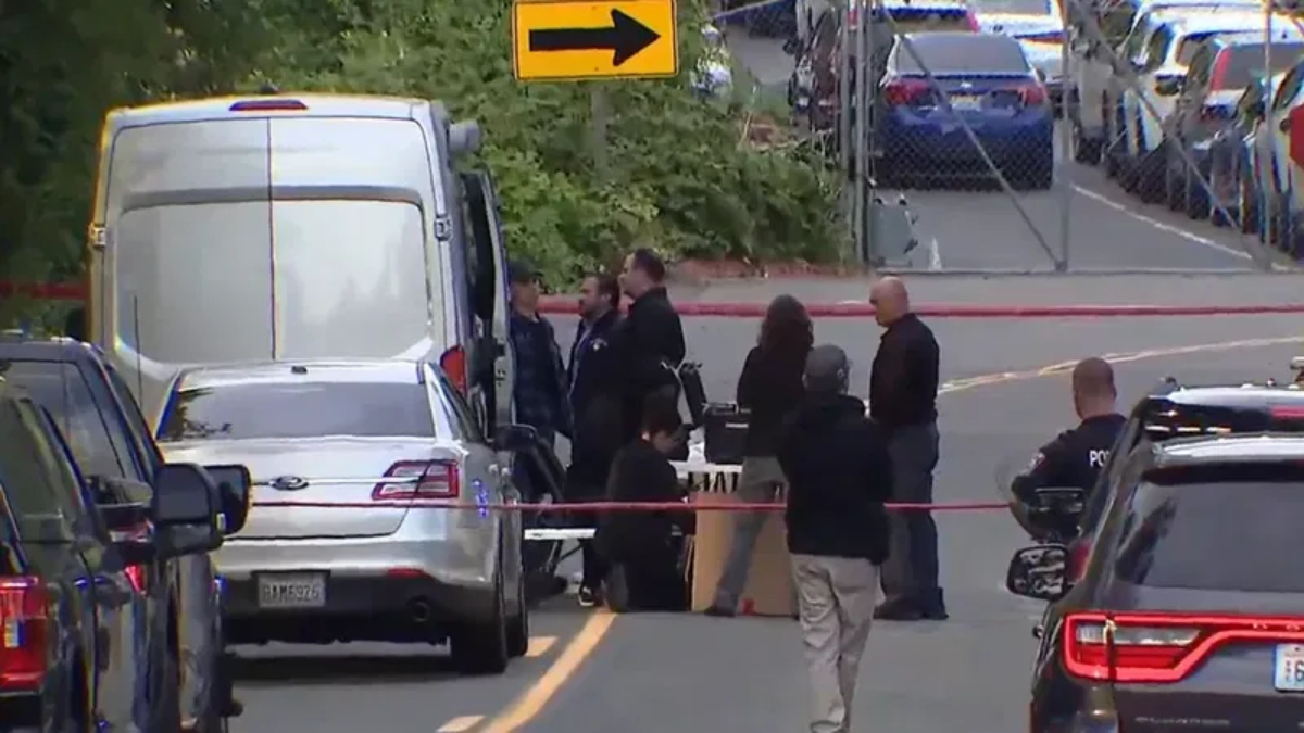 Group of people and police officers stand behind red caution tape around a white van on a city street, indicating an investigation scene.