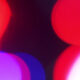 Abstract bokeh lights in red, pink, and purple against a dark background.