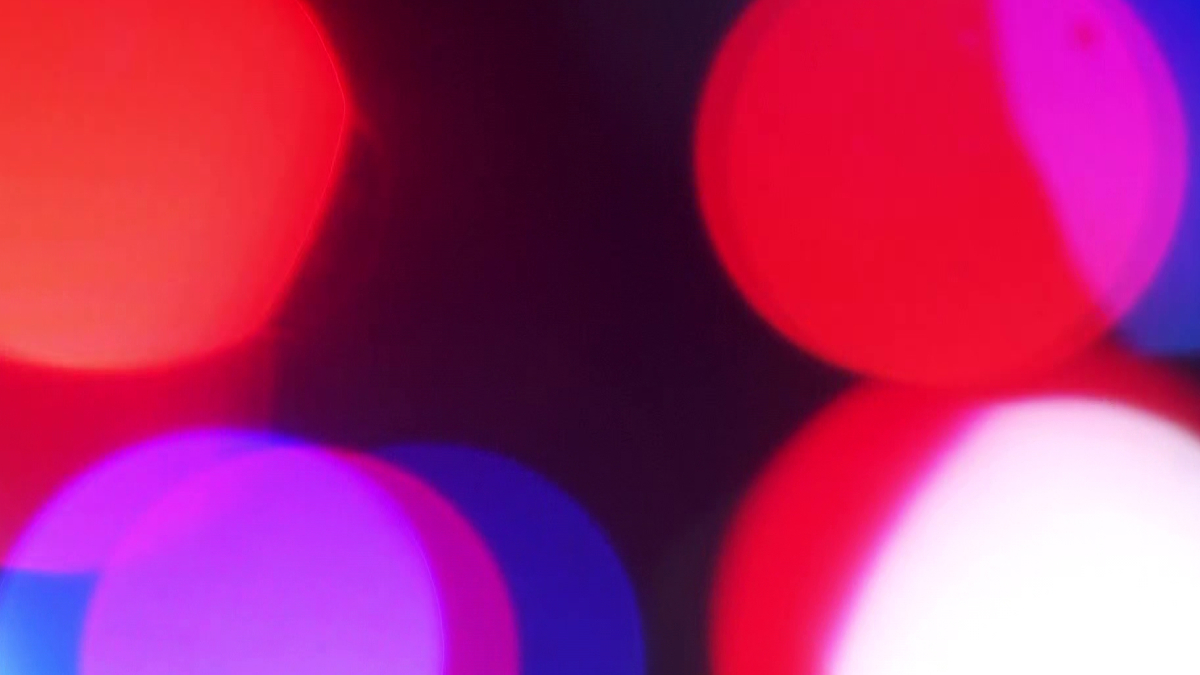 Abstract bokeh lights in red, pink, and purple against a dark background.