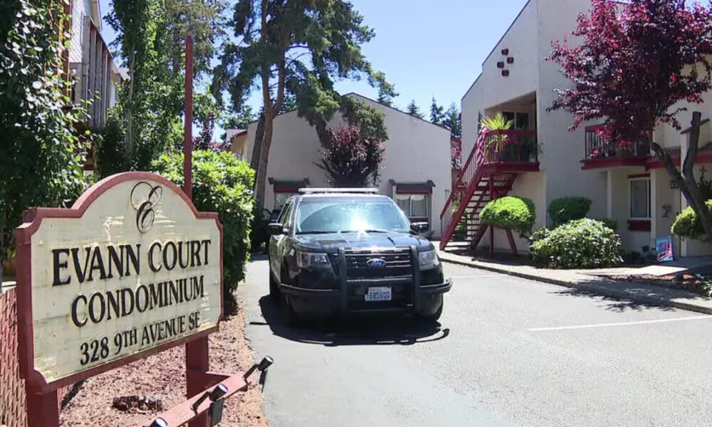 Sign reads Evann Court Condominium; a black SUV is parked in a driveway beside the red-stair apartment building and trees nearby.