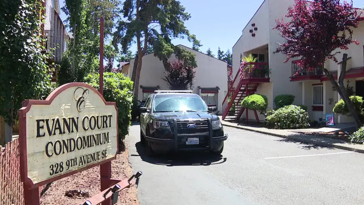 Sign reads Evann Court Condominium; a black SUV is parked in a driveway beside the red-stair apartment building and trees nearby.