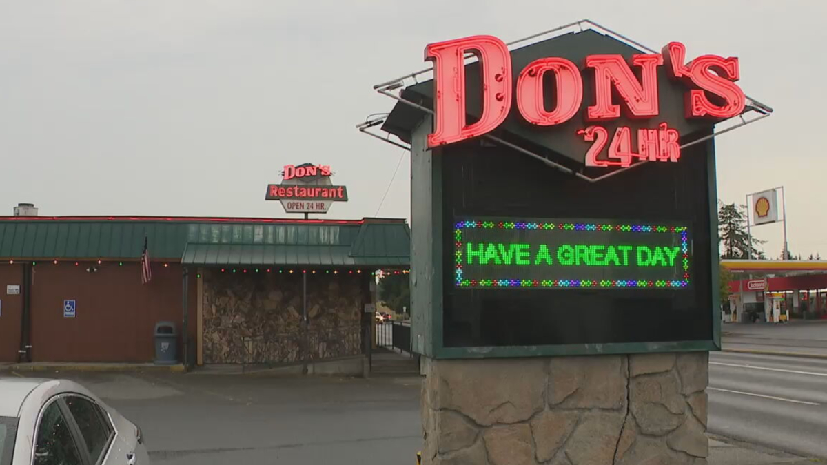 Don's 24 Hr neon sign atop a stone kiosk; LED board reads 'HAVE A GREAT DAY' with a diner and string lights in the background.