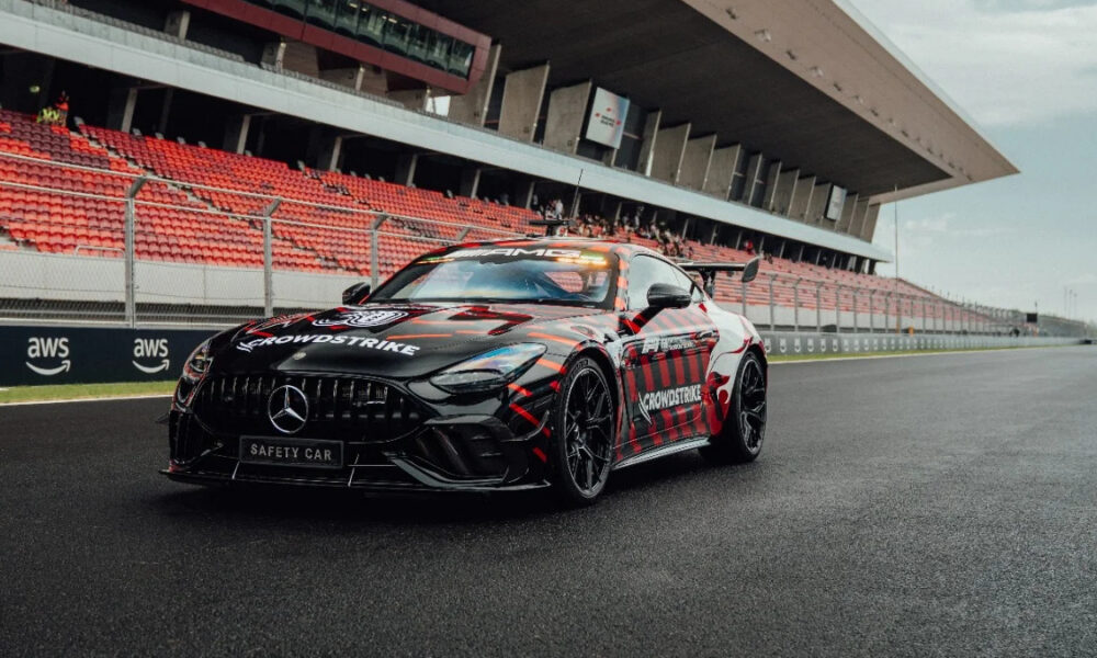 Black Mercedes AMG safety car with red graphics parked on a racetrack beside red-seated grandstands nearby.