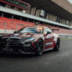 Black Mercedes AMG safety car with red graphics parked on a racetrack beside red-seated grandstands nearby.