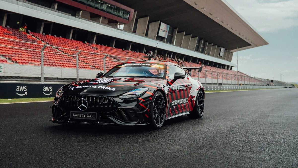 Black Mercedes AMG safety car with red graphics parked on a racetrack beside red-seated grandstands nearby.