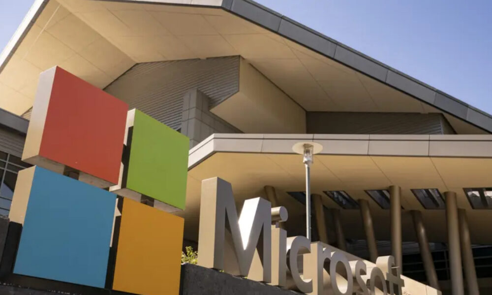 Exterior view of a Microsoft campus with a sculpture made of four colorful squares (red, green, blue, yellow) in front of a modern building.