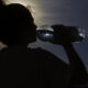 Silhouette of a person drinking from a water bottle outdoors at sunset, with a distant bird in the sky.