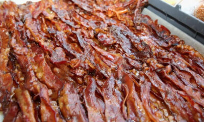 Tray filled with crispy, overlapping bacon strips glistening with fat.