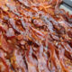 Tray filled with crispy, overlapping bacon strips glistening with fat.