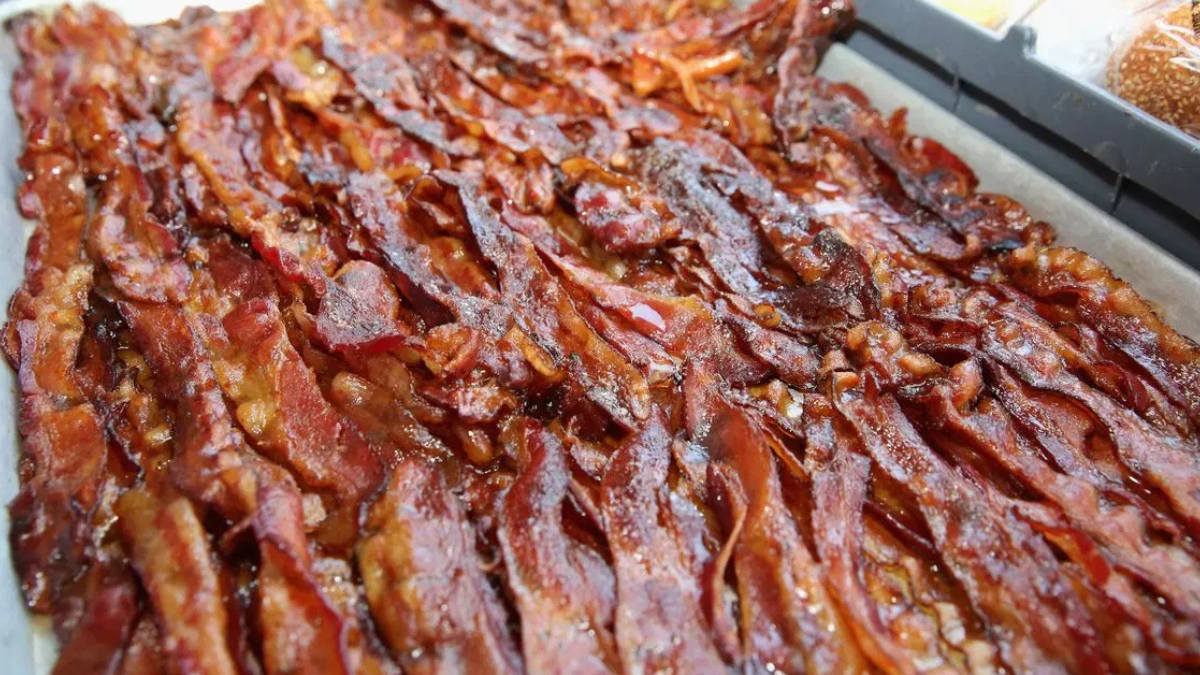 Tray filled with crispy, overlapping bacon strips glistening with fat.