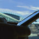Close-up of a person holding a smartphone outdoors with a stadium and blue sky in the background.