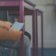 Student scrolling on a smartphone while seated in a classroom, purple chair legs visible nearby.