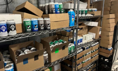 Storage shelf filled with spray paint cans and cardboard boxes in a workshop area.